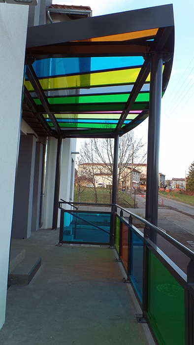 Marquise design aux panneaux de verre multicolores sur structure métallique, abritant un balcon avec garde-corps assorti.