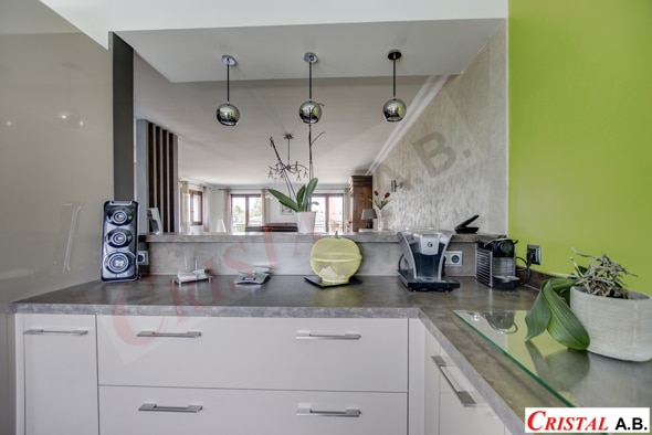 Cuisine moderne avec plan de travail gris, suspensions chromées et vue sur le séjour. Cristal A.B.