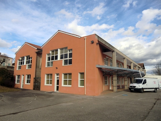 Bâtiment scolaire orange moderne aux grandes fenêtres avec un fourgon blanc stationné dans la cour.