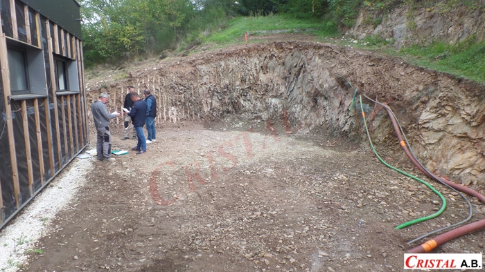 Chantier d'excavation avec paroi rocheuse, ouvriers étudiant des plans et gaines de réseaux. Logo CRISTAL A.B. visible.