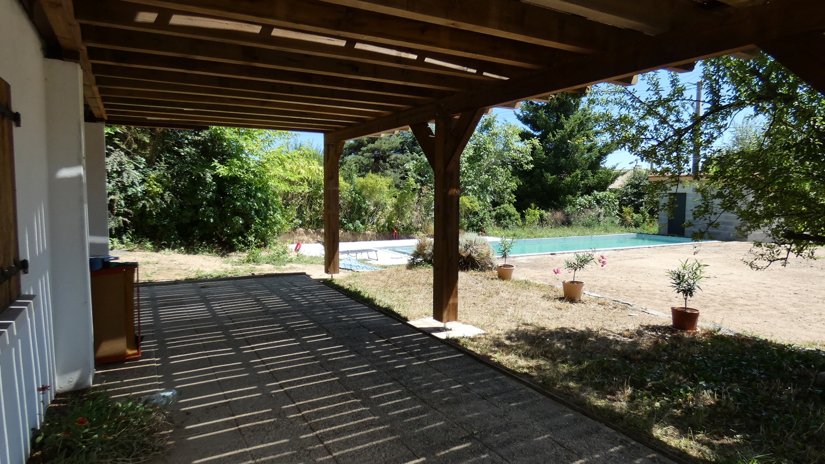 Terrasse carrelée sous une pergola en bois massif avec vue sur une piscine et un jardin verdoyant.
