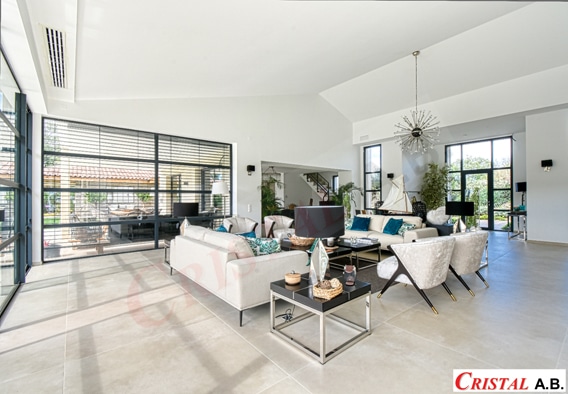 Salon moderne et lumineux avec mobilier design blanc, grandes baies vitrées et logo Cristal A.B.