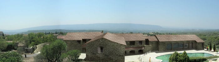 Villa en pierre avec piscine et vue panoramique sur les montagnes de Provence sous un ciel dégagé.