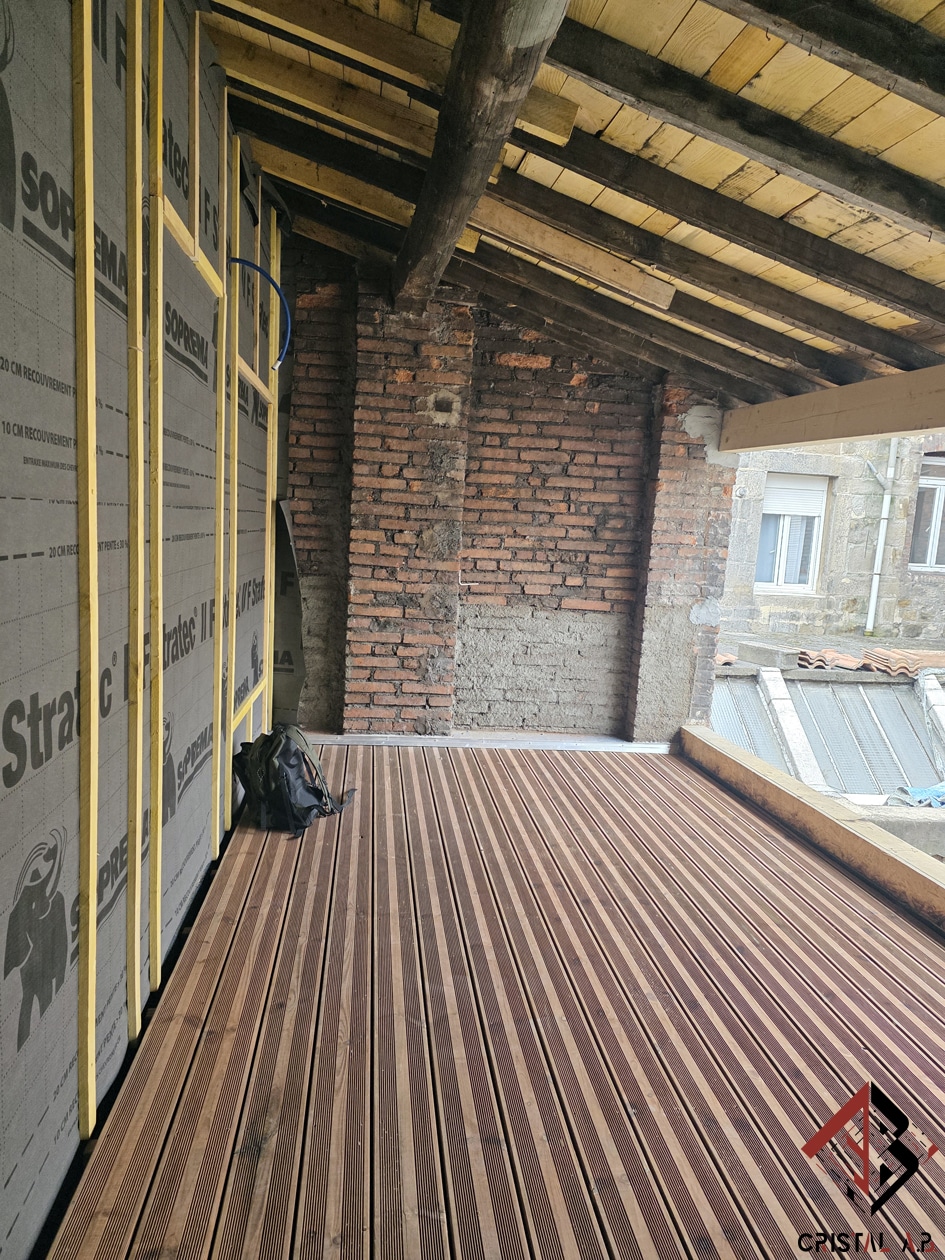 Aménagement d'une terrasse en bois avec isolation Soprema Stratec sur mur de briques en chantier de rénovation.